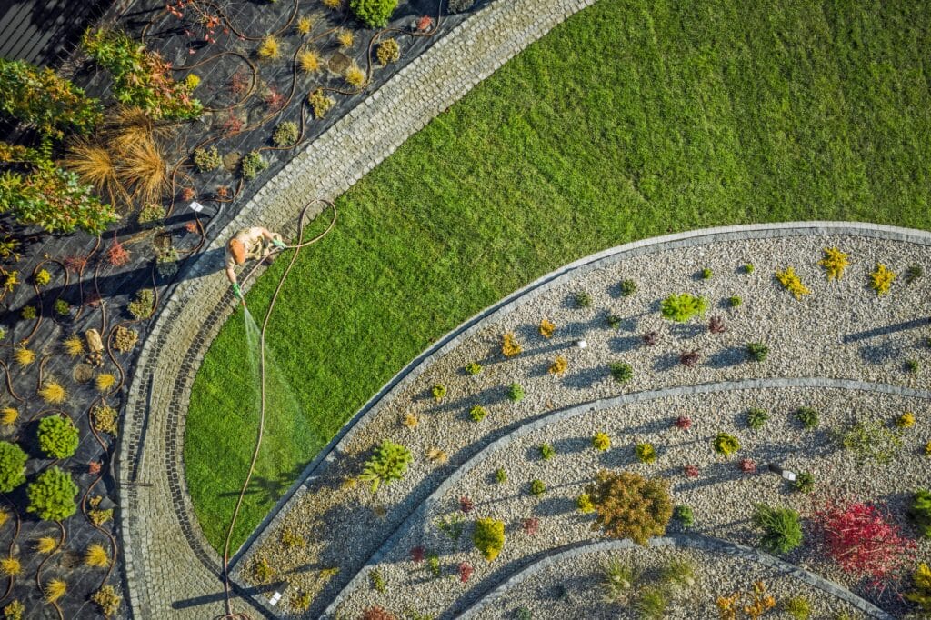 aerial shot of landscape design featuring local plants in firewise beds forming concentric circles. A lansdscaping professional is treating the lawn, wearing protective gear