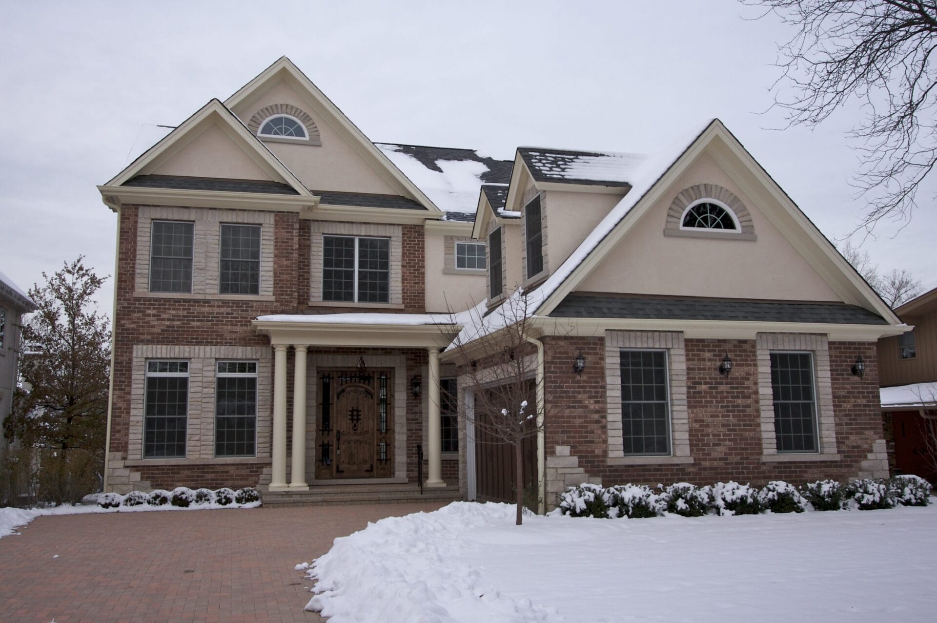 a two-story home with snow covering the front yard and plants