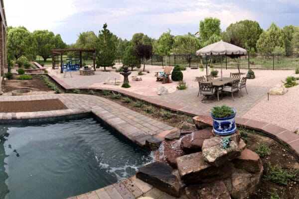 An outdoor living area designed by Zebrascapes including a hot tub with water feature, hardscape/patio area, and outdoor living/seating areas