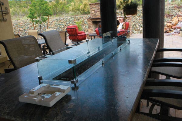 an outdoor dining area under a covered patio; an outdoor fireplace and water feature are visible in the background