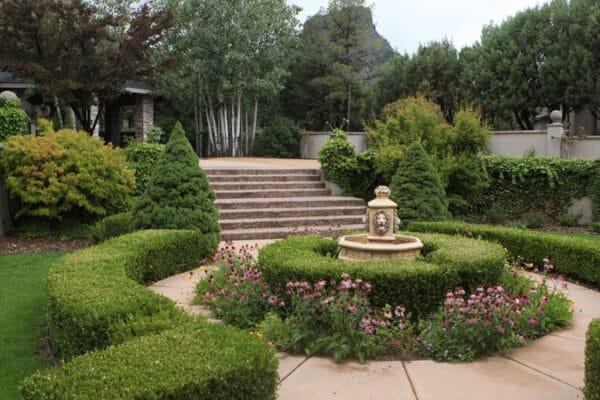 a lush outdoor living area featuring natural grass and green shrubbery/flowers surrounding an ornate fountain