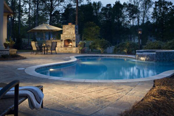 Zebrascapes custom pool area design installation featuring hardscapes, a water feature, and an outdoor fireplace with seating