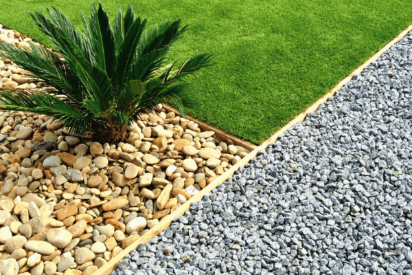 a close up a front yard refresh featuring a plant in brown stones, green grass, and a gravel path
