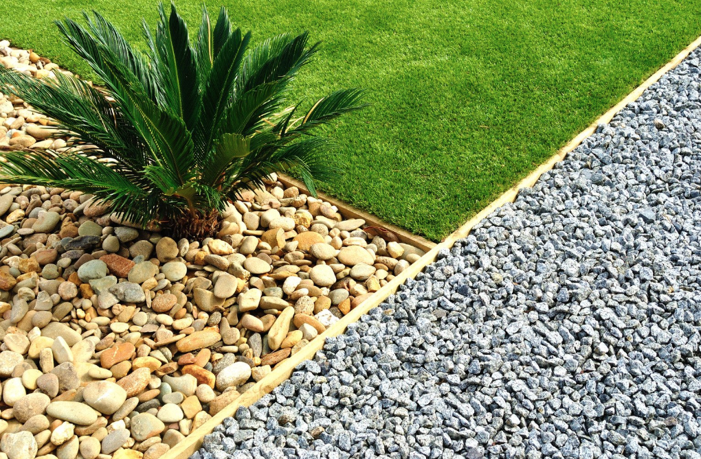 a close up a front yard refresh featuring a plant in brown stones, green grass, and a gravel path