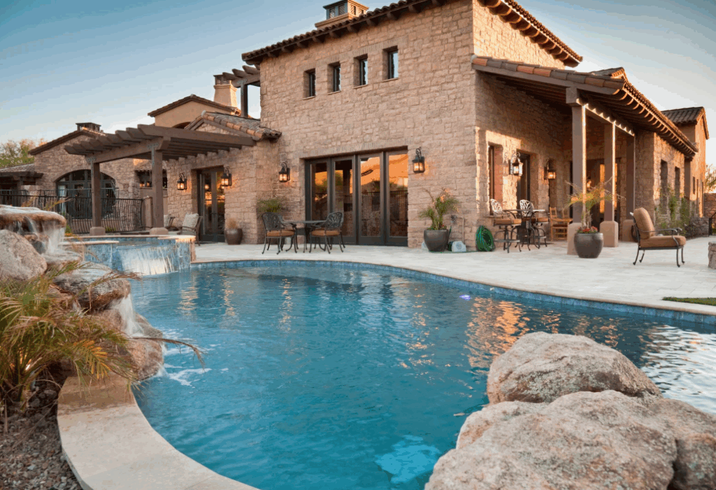 a pool with a luxury stucco home in the background and hardscapes framing it